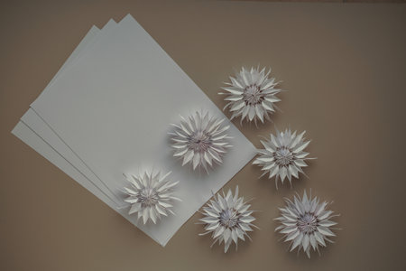 Blank sheets of paper with copy space and flowers made of paper close-up view from above DIY on...