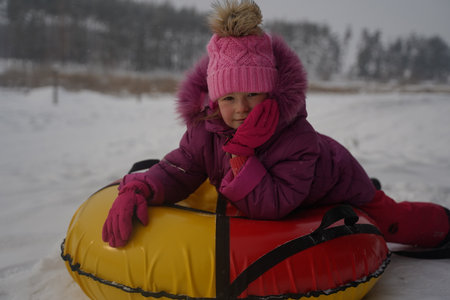 Cute little girl enjoying sledding in the snow close-up. children slides. The kid is riding a sleigh...