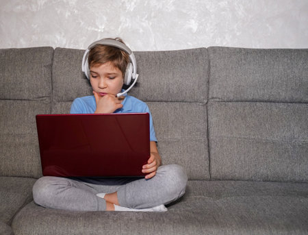 Portrait of little boy in wireless headset with laptop, online studying at homeの写真素材