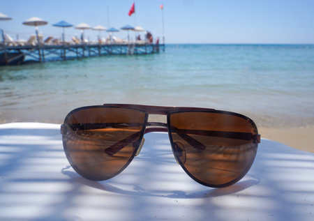 Sunglasses lie on a plastic table on the beach, against the backdrop of the seaの写真素材
