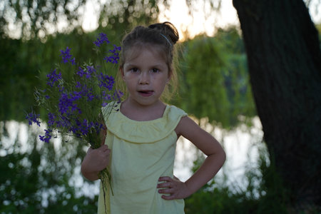 A hippy girl holding a bouquet of wildflowers in her hands. Little Girl holds large bouquet of purple lupins. nature concept. present.の写真素材