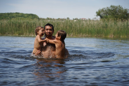 Dad holds his sons standing in the river. Everyone is laughing and having fun