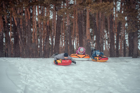 Children and parents have fun riding from the snowy mountain on tubing. Group of children sliding down on tubesの写真素材