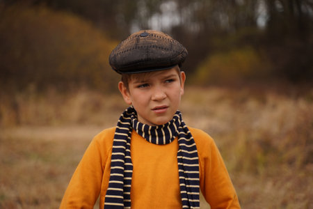 Portrait of a cute teenager in a retro cap and a striped scarf against the backdrop of an autumn...