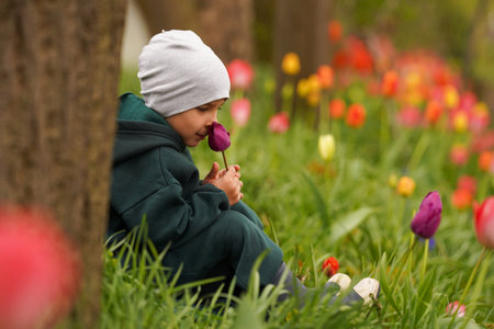 Cute child sitting in the autumn garden and sniffing the purple bud of a tulip. baby boy outdoors in the gardenの写真素材