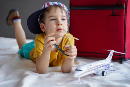A little boy lies next to a suitcase and dreams of a summer vacation. Waiting for the holidays. Travel and adventure conceptの写真素材