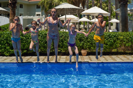 The family has fun jumping into the swimming pool. Mom and children in flight over the swimming pool. A fun family vacationの写真素材