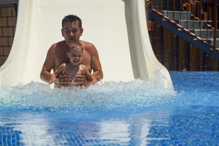 Happy child with dad goes down the water slide in the water park, around a cloud of spray. happy...