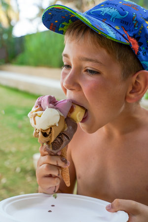 A child with an appetite eats a huge multi-colored ice cream on a summer vacation. Tropical vacations, family vacations at the hotel.の写真素材