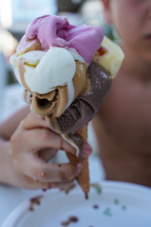Large multi-colored ice cream in a waffle cone in the child's hand, focus on ice cream, the child is...