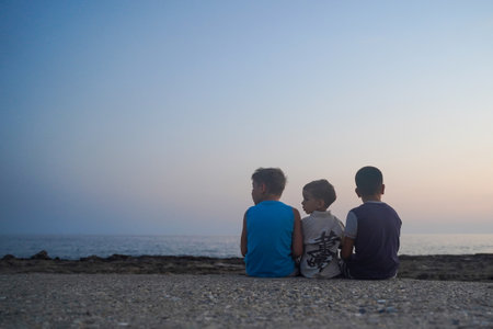 Rear view of children sitting in front of the sea and looking sideways, copy spaceの写真素材
