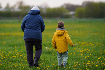 Grandma walking with her grandson through a spring field of dandelions, happy retirement, rear viewの写真素材
