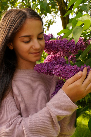 Cute girl in purple dress posing with lilac flowers. Portrait of little girl with lilac, spring moodの写真素材
