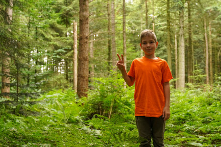 A teenager shows a symbol of peace and victory while standing in the forest. The concept of peace and environmental protection. well-being symbolizingの写真素材