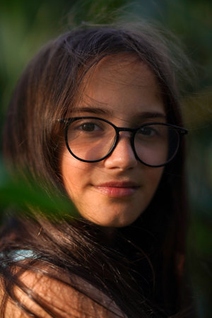 Portrait of a brunette girl wearing glasses on a green blurred backgroundの写真素材