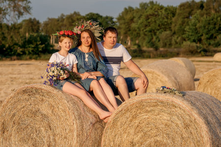 Happy parents and daughter in a summer field on a haystack. Mom with dad and children in the field. Happy parentingの写真素材