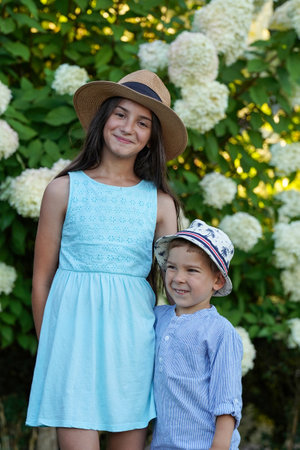 A boy and a girl in retro hats and summer clothes have fun on a blooming background. A fun family vacationの写真素材