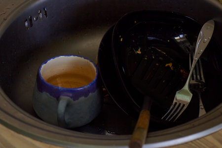Dirty dishes after eating in the sink. Ceramic cup with tea, black plates and metal forks. No dishwasher. cleaning and housework.の写真素材