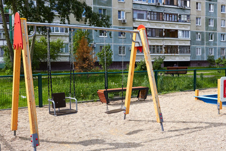 Photo of children's swing on iron chains playground next to multi-storey building. Recreation and entertainment for children.の写真素材
