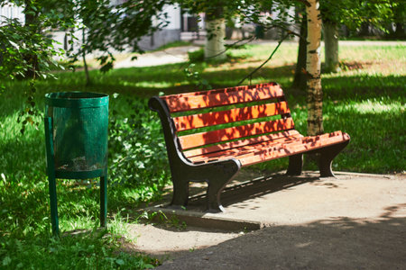 bench and green trash can in city park.
