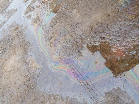 Spill of petrol in the road puddle. Gasoline footprint rainbow on the asphalt. Concept of ecological problem of environmental pollution. Multicolored streaks, reflection of houses and wiresの写真素材