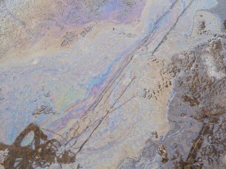 Spill of petrol in the road puddle. Gasoline footprint rainbow on the asphalt. Concept of ecological problem of environmental pollution. Multicolored streaks, reflection of houses and wiresの写真素材