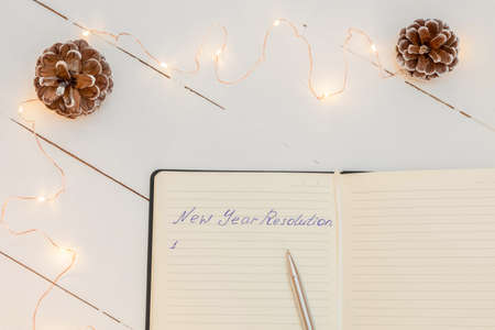Notepad with handwritten text New Year Resolution on white wooden table and Christmas decorations