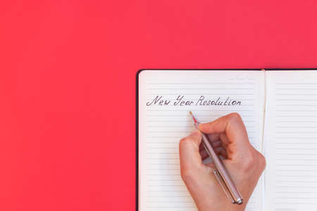 Directly above view of woman's hand writing words New Year Resolution in a notepad on red background, copy spaceの写真素材