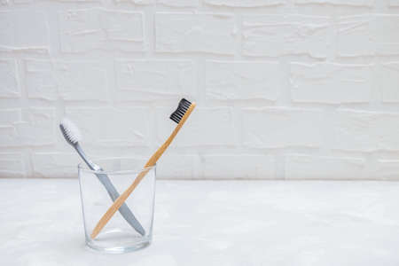 Plastic toothbrush and eco-friendly bamboo toothbrush in a glass cup on grey neutral background, copy space. No plastic conceptの写真素材