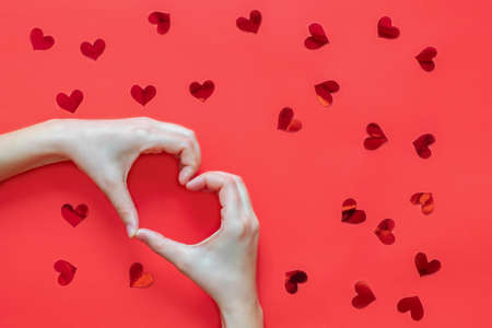 Woman hands making heart shape on red background with red red heartsの写真素材