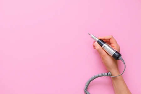 Woman hand holding electric nail manicure machine pen on pink backgroundの写真素材