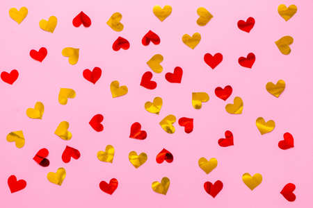 Red and golden scattered paper hearts confetti on pink background