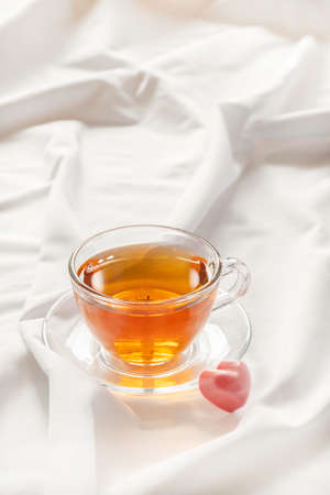 Romantic mood concept. Cup of tea with heart shaped pink candy on white bed with copy space.の写真素材
