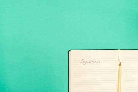 Expense calculation concept. Top view of pen and notepad with handwritten words Expenses on green background with copy spaceの写真素材
