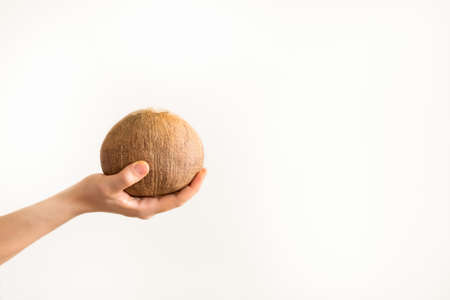 Woman hand holding a coconut nut on white neutral background with copy spaceの写真素材