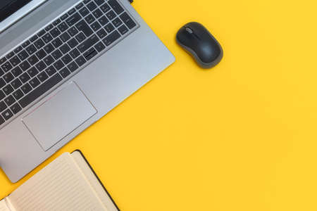 Top view of workspace with laptop and notepad on bright yellow background with copy spaceの写真素材