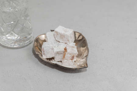 Lokum in metallic plate with glass of water on concrete background