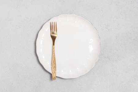 Directly above view of golden fork with white plate on neutral concrete background with space for...