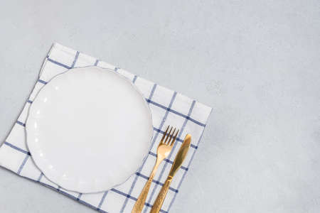 Cutlery background with white empty plate and golden knife and fork on neutral background. Top view...