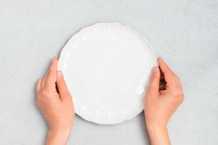 Young woman hands holding white empty plate on neutral concrete background. Image with copy space, top viewの写真素材