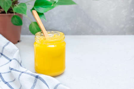 Ghee or clarified butter in a glass jar on a neutral textured background