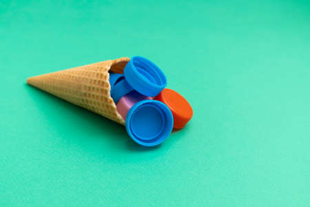 Plastic free and unnatural plastic food concept. Waffle cone with plastic bottle caps on green...
