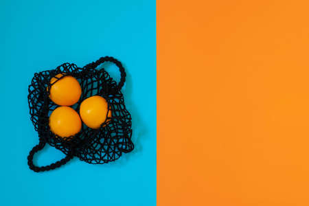 Zero waste concept. Black mesh shopping bag with oranges on blue and orange color geometric...