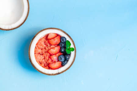 Top view of berry smoothie in a coconut bowl with fresh strawberries and blueberries, mint leaves on blue background with copy spaceの写真素材