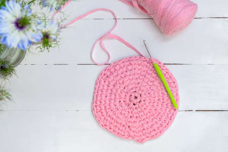 Crocheting and home hobby concept. Top view of crochet work with crochet hook and pink yarn on white...