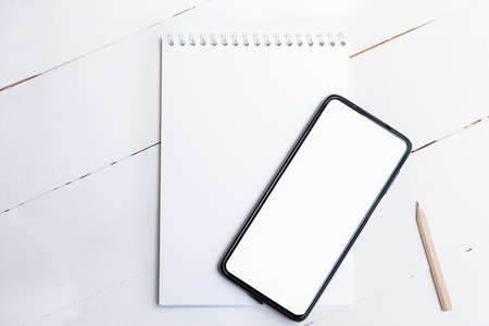 Top view of blank smartphone with white screen on paper notepad on white wooden backgroundの写真素材