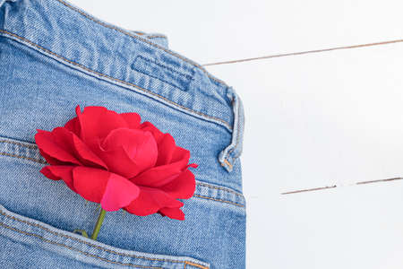 Flat lay with blue jeans and red rose flower on white wooden table. Spring clothing and accessories conceptの写真素材