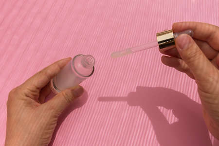 Woman hands holding bottle with collagen serum on pink background with creative shadowsの写真素材