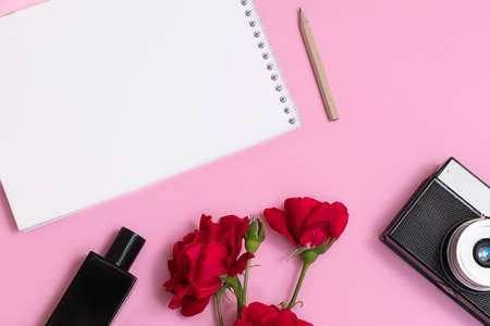 Top view of flat lay with empty blank notepad, pen, red flowers, retro photo camera, perfumの写真素材