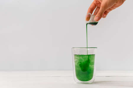 Woman hand pouring liquid chlorophyll in a glass cup. White background with space for textの写真素材